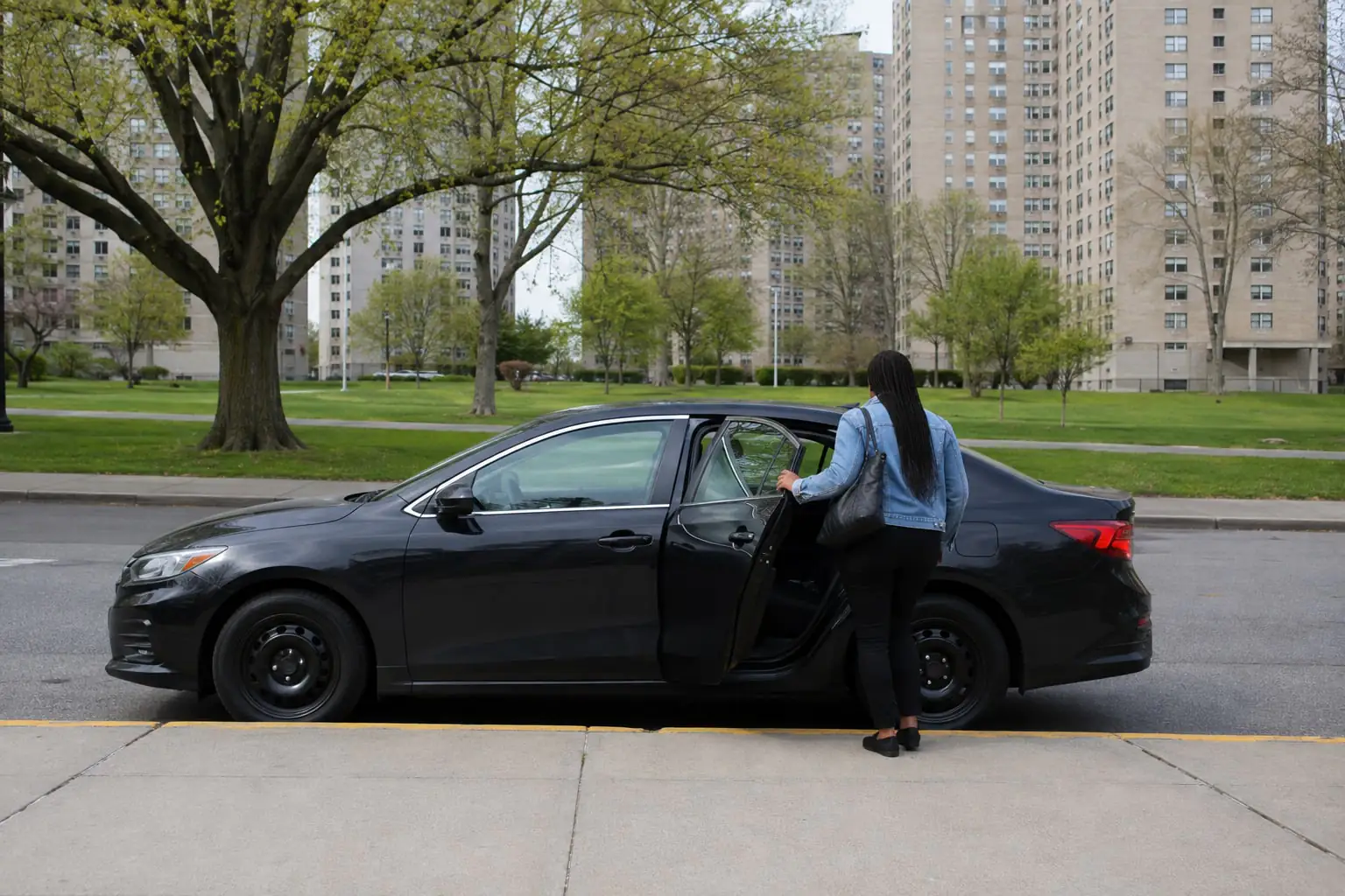 Passenger entering a sedan beside apartment towers and lawns, illustrating a Co-op City NY rideshare pickup.