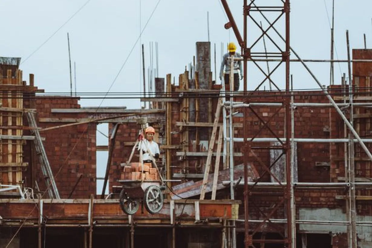 Construction worker on a scaffold at a building site with cranes and brickwork