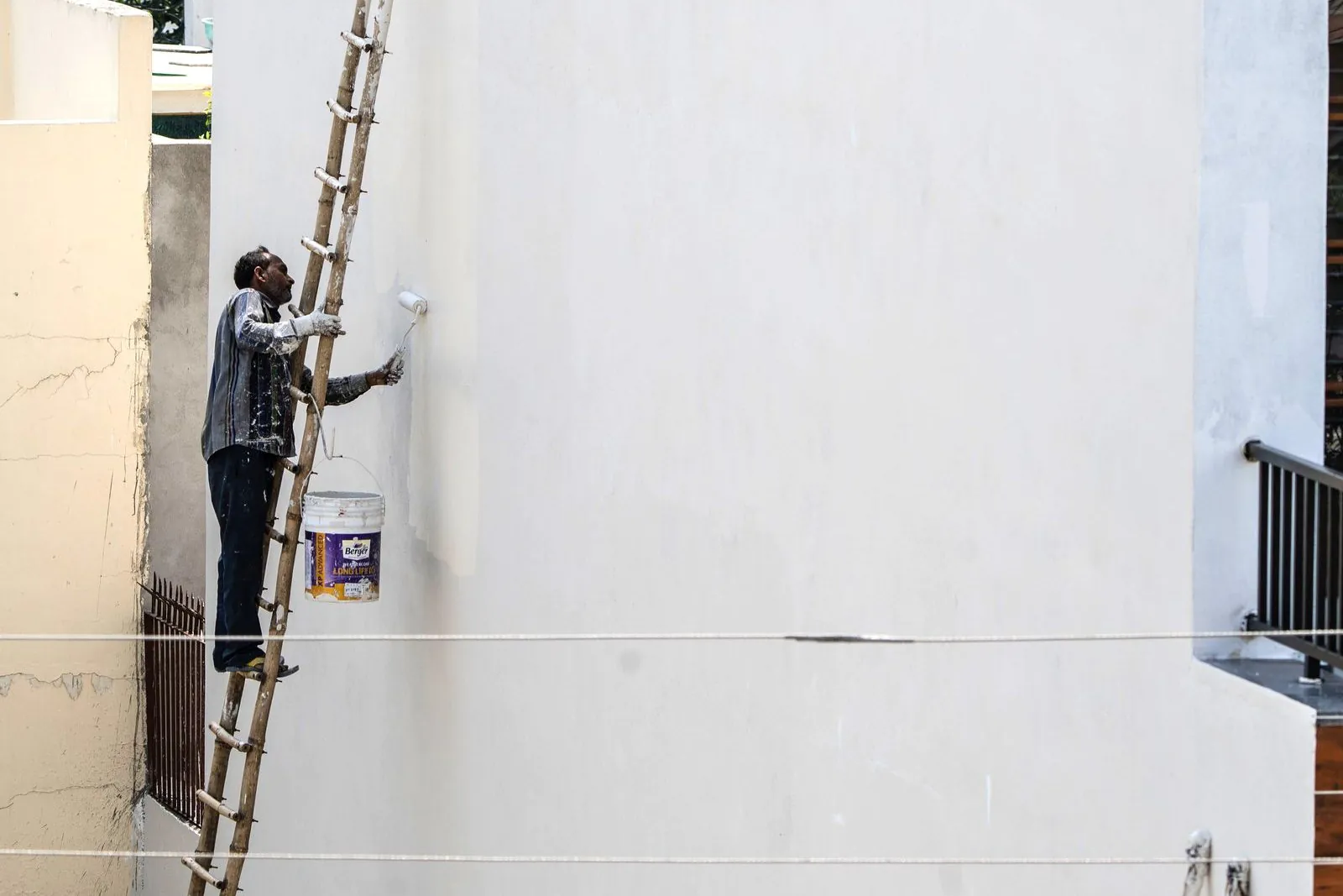 Worker painting a building exterior while standing on a tall ladder