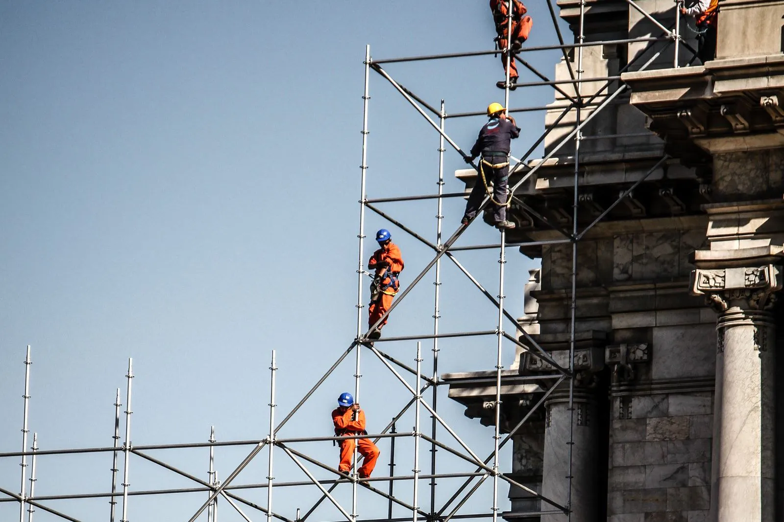 Construction workers climbing a tall scaffolding tower