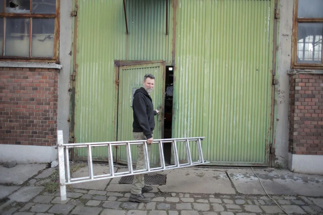 Worker carrying a stepladder into a warehouse doorway in the city