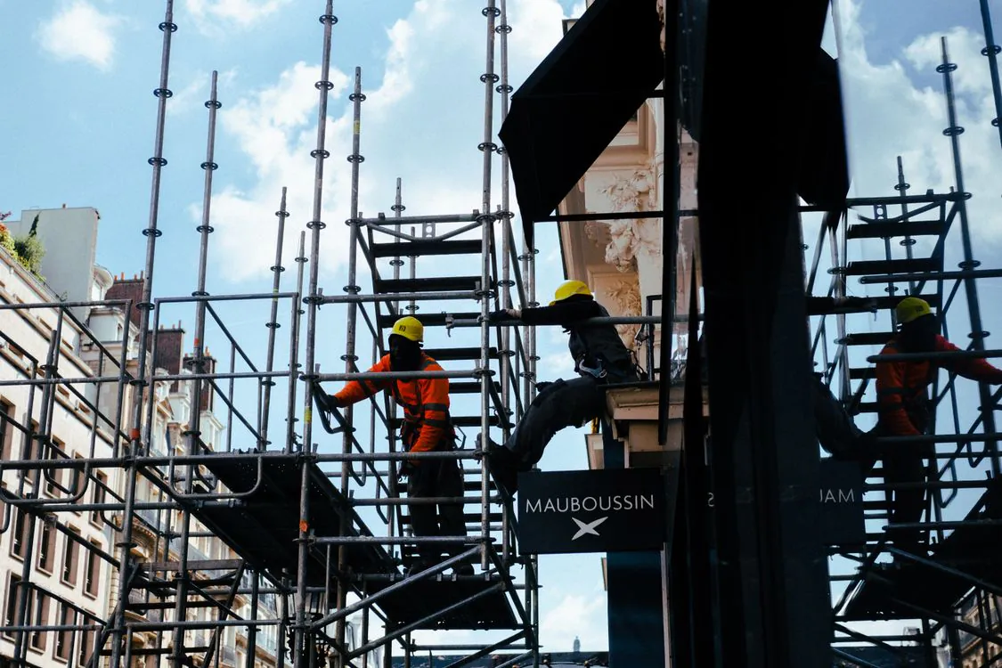 Construction workers silhouetted on scaffolding against a city sky