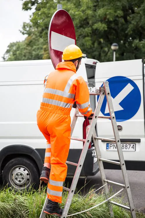 Worker in orange safety gear working from a ladder at a jobsite