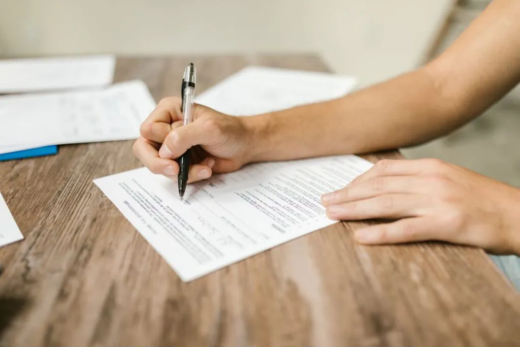 Close-up of a hand filling out a claim form with a pen